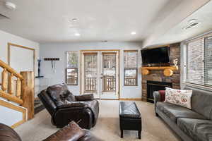 Living room featuring baseboards, visible vents, stairs, a stone fireplace, and carpet floors