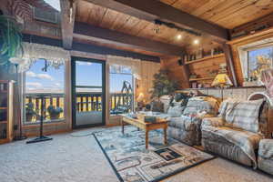 Carpeted living area featuring beamed ceiling, visible vents, wood walls, rail lighting, and wood ceiling