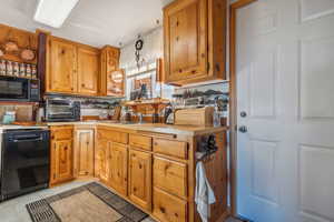 Kitchen featuring a toaster, light countertops, light tile patterned floors, brown cabinetry, and black appliances