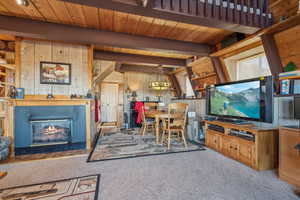 Carpeted living room featuring beam ceiling, wooden walls, wood ceiling, and a glass covered fireplace