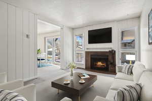 Living area featuring carpet floors, a tiled fireplace, a textured ceiling, and wood walls