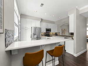 Kitchen featuring a kitchen bar, a peninsula, stainless steel appliances, white cabinetry, and dark wood-style flooring