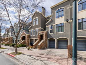 View of property featuring a residential view, concrete driveway, stucco siding, stone siding, and an attached garage
