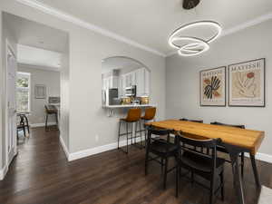 Dining room featuring crown molding, baseboards, arched walkways, an inviting chandelier, and dark wood-style floors