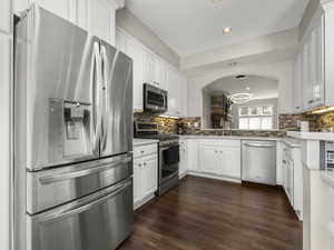 Kitchen featuring backsplash, dark wood finished floors, stainless steel appliances, white cabinetry, and a sink