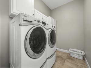 Laundry room featuring cabinet space, washing machine and dryer, baseboards, and light tile patterned flooring