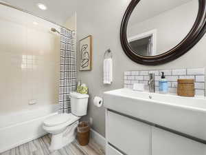 Bathroom with baseboards, toilet, decorative backsplash, shower / bath combination with curtain, and vanity