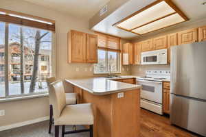 Kitchen featuring a breakfast bar area, light brown cabinets, a peninsula, white appliances, and a sink