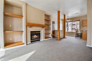 Unfurnished living room with carpet, built in shelves, baseboards, and a fireplace with flush hearth