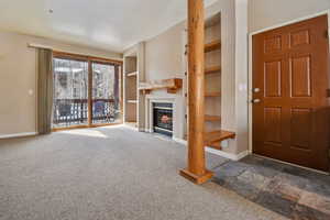 Unfurnished living room with built in shelves, dark carpet, a glass covered fireplace, and baseboards