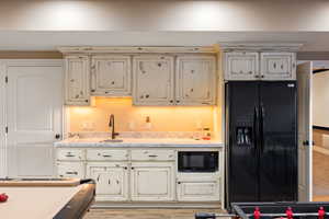 Kitchen with light stone countertops, cream cabinets, black appliances, and a sink