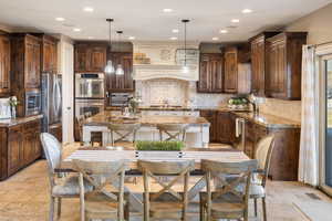 Kitchen featuring an island with sink, backsplash, stone tile flooring, and appliances with stainless steel finishes