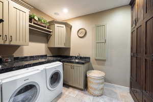 Laundry area with a sink, washing machine and dryer, stone tile flooring, cabinet space, and baseboards