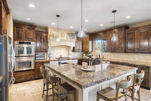 Kitchen with stone tile flooring, stainless steel appliances, a kitchen bar, and a kitchen island with sink