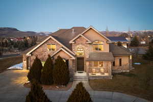 View of front of home featuring driveway, a shingled roof, stucco siding, stone siding, and a mountain view