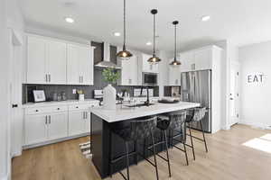 Kitchen featuring tasteful backsplash, a sink, wall chimney range hood, stainless steel appliances, and a kitchen island with sink