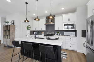 Kitchen with a sink, appliances with stainless steel finishes, wall chimney exhaust hood, light countertops, and decorative backsplash