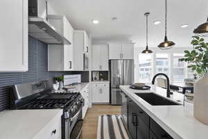 Kitchen with light countertops, decorative backsplash, appliances with stainless steel finishes, wall chimney exhaust hood, and a sink