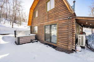 View of snowy exterior featuring log exterior, central AC, and a hot tub