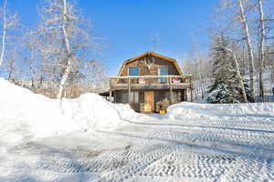 Snow covered rear of property featuring a gambrel roof and a wooden deck