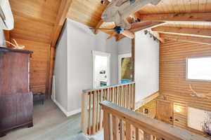 Hallway with baseboards, vaulted ceiling with beams, wood ceiling, an upstairs landing, and rustic walls