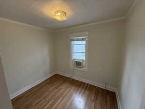 Empty room with wood finished floors, baseboards, and ornamental molding