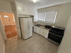 Kitchen with light tile patterned flooring, stainless steel range with gas stovetop, freestanding refrigerator, a sink, and white cabinetry