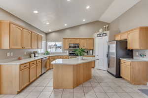 Kitchen with light brown cabinetry, appliances with stainless steel finishes, a center island, and light countertops