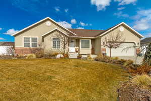 Ranch-style home with stucco siding, a front lawn, concrete driveway, a garage, and brick siding