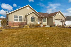 Ranch-style house with a front lawn, an attached garage, brick siding, and stucco siding