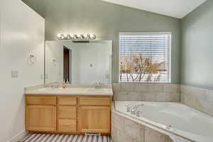 Bathroom with double vanity, a garden tub, lofted ceiling, and a sink