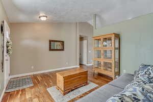 Living area featuring vaulted ceiling, a textured ceiling, baseboards, and wood finished floors