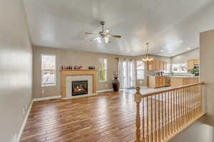 Living area with baseboards, lofted ceiling, a fireplace, light wood-style floors, and ceiling fan with notable chandelier