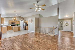 Unfurnished living room featuring light wood-type flooring, lofted ceiling, baseboards, and ceiling fan with notable chandelier