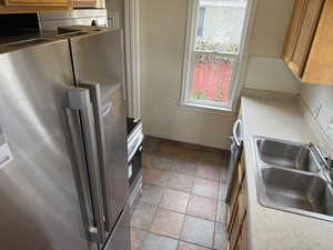 Kitchen featuring a sink, stone finish flooring, freestanding refrigerator, light countertops, and decorative backsplash