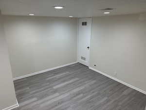 Spare room with visible vents, a textured ceiling, baseboards, and wood finished floors