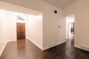 Hall featuring dark wood finished floors, vaulted ceiling, baseboards, and visible vents