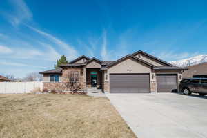 View of front of property featuring stone siding, fence, concrete driveway, a front yard, and a garage