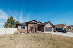 View of front facade with stone siding, driveway, an attached garage, and a gate