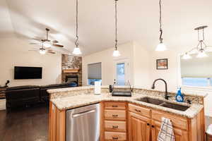 Kitchen with light brown cabinetry, a stone fireplace, dark wood-type flooring, a sink, and open floor plan