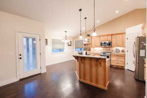 Kitchen featuring a kitchen bar, light brown cabinetry, light stone counters, dark wood-style floors, and appliances with stainless steel finishes