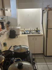 Kitchen with light countertops, light tile patterned floors, freestanding refrigerator, and a sink