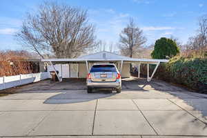 View of parking with driveway, a carport, and fence