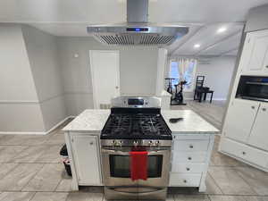 Kitchen featuring white cabinetry, range hood, baseboards, and gas range