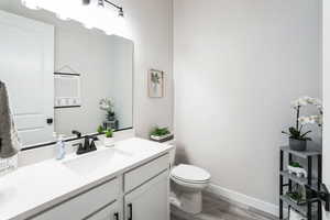 Half bathroom with toilet, vanity, baseboards, and wood finished floors