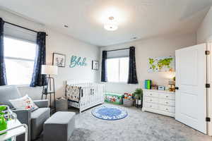 Carpeted bedroom featuring visible vents, a textured ceiling, and a crib