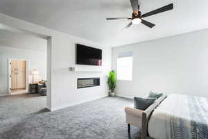 Carpeted bedroom with a glass covered fireplace, a textured ceiling, baseboards, and a ceiling fan