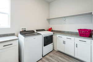 Laundry area featuring light wood finished floors, cabinet space, and washing machine and clothes dryer