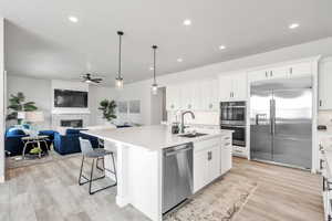 Kitchen with light wood finished floors, a sink, appliances with stainless steel finishes, a glass covered fireplace, and open floor plan
