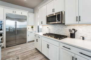 Kitchen featuring light wood-type flooring, appliances with stainless steel finishes, white cabinetry, and light countertops